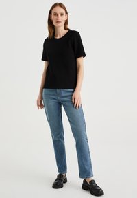 Czarny krótki t-shirt z okrągłym dekoltem, zestawiony z jasnoniebieskimi dżinsami o prostym kroju i czarnymi ciężkimi mokasynami. Prosty, casualowy strój.