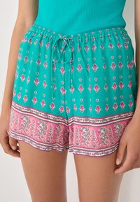 Shorts turquoise légers avec une taille à cordon, ornés d'un motif floral rose et de bordures décoratives. Tissu doux et respirant.