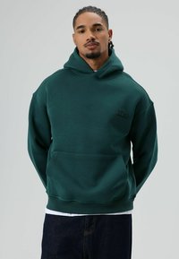 Sweat à capuche en polaire verte avec une poche avant et un logo brodé "ZERO", doté d'une capuche à cordon de serrage et de poignets côtelés. Texture lisse.