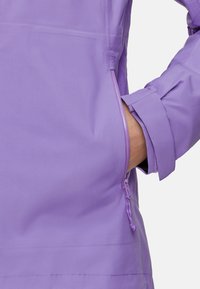 Chaqueta de color lila claro con un bolsillo con cremallera y puños ajustables. La tela tiene una textura sutil, con un aspecto suave y ligero.