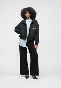 Čierna skrátená bunda, svetlomodrá košeľa, široké čierne nohavice a čierne špicaté lodičky. Bunda má logo a voľný strih.