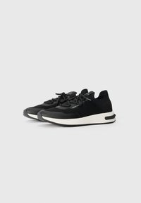 Pantofi sport negri cu un superior din tricot, talpă flexibilă și o talpă intermediară albă contrastantă. Au vârf rotund și sistem de șireturi la față.