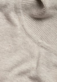 Hellbeige Strickstoff mit einer glatten Textur und gerippten Akzenten. Der Stoff scheint weich zu sein und hat einen leicht schimmernden Effekt. Subtile Farbvariationen sind vorhanden.
