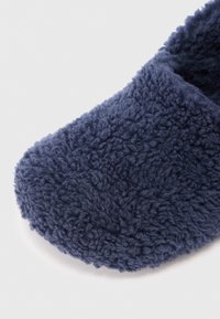 Acercamiento de una suave pantufla de forro polar azul marino con punta redondeada sobre un fondo blanco.