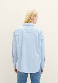 Camisa de botão azul às riscas, feita de algodão, com mangas longas e colarinho. Apresenta riscas horizontais e um corte relaxado.