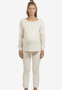 Cremfarbener Strickpullover mit weitem Ausschnitt und langen Ärmeln, kombiniert mit figurbetonten cremefarbenen Hosen, die eine subtile Textur aufweisen.