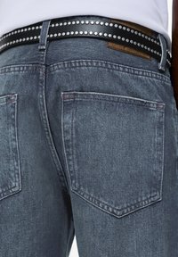 Mörkgrå denimjeans med en lätt urtvättad textur, utrustad med två bakfickor och ett svart bälte prytt med silvernitar.