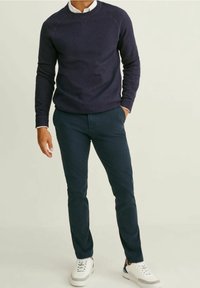 Marinblå texturerad tröja med rund halsringning, matchad med mörkgröna chinos och vita sneakers. Avslappnad, åtsittande design med kontrasterande stilar.