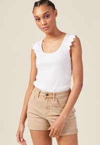 Vit ribbad linne med scalloped ärmar och beige denimshorts. Shortsen har en uppvikt nederkant och knappstängning. Neutral, minimalistisk design.