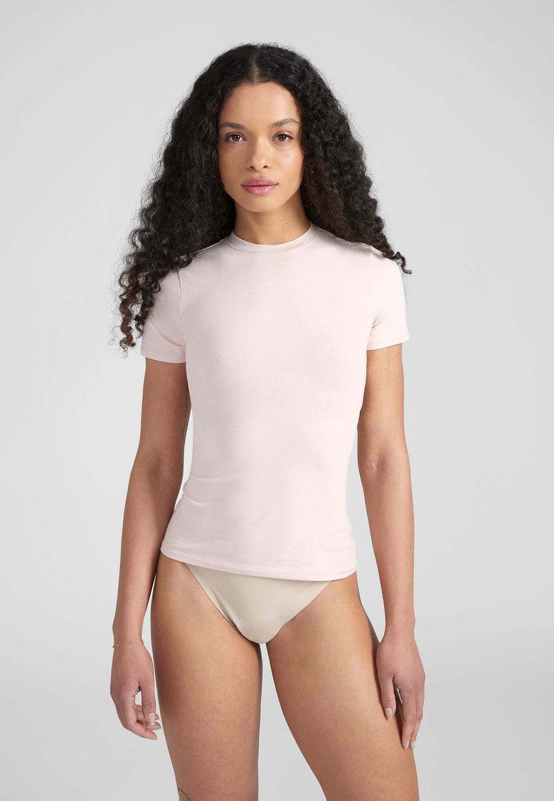 T-shirt aderente a maniche corte in tessuto rosa chiaro con scollo rotondo, texture liscia e design minimale.