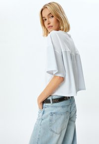 Weiß gestreifter, hellblauer Cropped-Top mit weiten Ärmeln, ergänzt durch einen schwarzen Gürtel und hellblaue hochtaillierte Jeans.