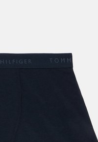 Navy blue cotton boxer brief with a dark waistband featuring embossed "TOMMY HILFIGER" logo. Smooth texture with a noticeable seam detail.