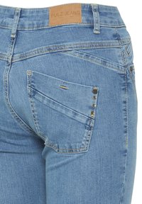 Svijetloplave traperice s visokim strukom, s dizajnom stražnjeg džepa s dijagonalnim linijama i tri ukrasne metalne zakovice.