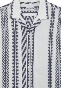 Chemise col en tissu léger ornée de motifs géométriques navy complexes sur fond blanc ; cinq boutons sur le devant.