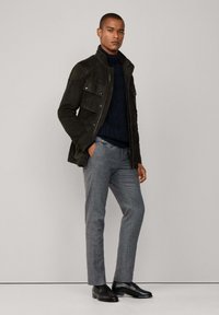 Tamnozeleni zamak od antilopa s prednjim džepovima, nosi se preko mornarskoplavog pletenog džempera. Sivi krojeni hlače i crne cipele upotpunjuju izgled.