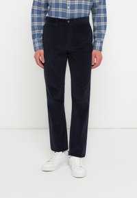 Navy corduroy broek met een rechte pasvorm, textuurstof en een knoopsluiting. Gecombineerd met witte sneakers en een blauw geruit shirt.