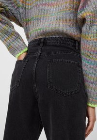 Jeans in denim nero con vita alta, dotati di tasche posteriori e una leggera texture. Abbinati a un maglione lavorato a maglia multicolore.