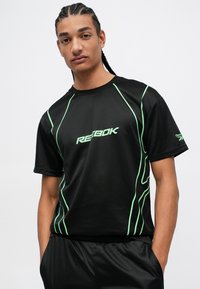 Čierne atletické tričko s zelenými akcentovými líniami a logom "Reebok" na prednej strane. Krátke rukávy a voľný strih pre pohodlie.