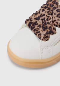 Λευκό συνθετικό αθλητικό παπούτσι με στρογγυλεμένη μύτη, διακοσμημένο με κορδέλα με λεοπάρ σχέδιο και ελαφριά καφέ λαστιχένια σόλα.