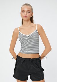 Top corto de rayas blancas y negras con tirantes finos y escote en V, combinado con pantalones cortos negros con cordón. Textura suave y diseño ajustado.