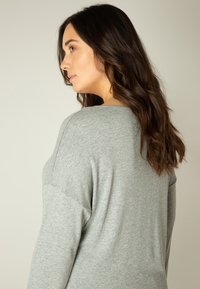 Grauer Pullover aus weichem Stoff mit lockerer Passform. Verfügt über einen runden Halsausschnitt und heruntergesetzte Schulternähte. Glatte Textur.