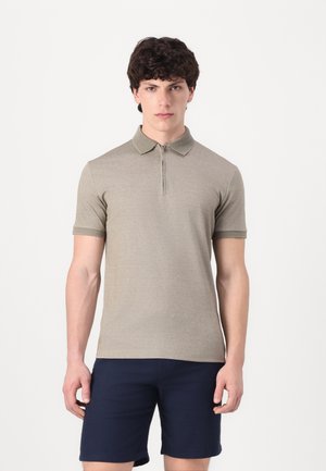 Kortermet polo-skjorte i lys beige. Har glidelås på kragen, teksturert stoff og slim fit, kombinert med marineblå shorts.