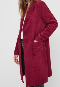 Abrigo de pana burdeos con un cierre de un solo botón, solapas con muesca, bolsillos delanteros y mangas largas. Tejido texturizado acanalado.