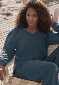 Conjunto de salón texturizado en azul que incluye una blusa de cuello en V y pantalones a juego. La tela tiene un patrón acanalado y un ajuste holgado para mayor comodidad.
