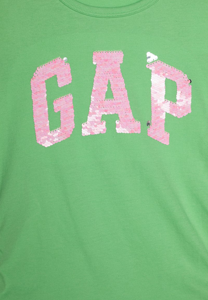 Grünes Baumwoll-T-Shirt mit pinken Pailletten-"GAP"-Logo. Kurze Ärmel, runder Ausschnitt, glatte Textur. Keine besonderen Akzente.