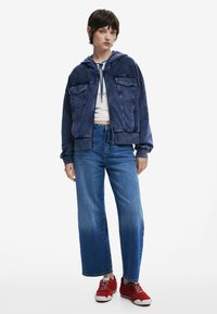 Navyblaue, fleecegefütterte Kapuzenjacke mit zwei Fronttaschen, kombiniert mit hochtaillierten blauen Jeans und roten Sneakers. Lässiges, entspanntes Design.