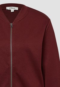 Bordeaux sweatshirt met een ritssluiting aan de voorkant, ronde halslijn en lange mouwen. Gemaakt van een zachte, gestructureerde stof met een gladde ritsaccent.