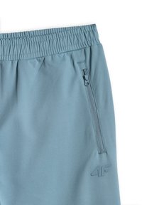 Pantalon de sport bleu clair avec taille élastique, poche latérale zippée et logo "4F" embossé près de la poche.