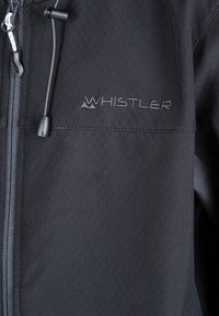 Sort jakke lavet af struktureret stof med lynlås og snøre, med "WHISTLER" broderet på brystområdet.