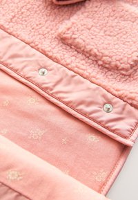 Różowa kurtka z teksturowanym, polarnym górnym panelem, satynową podszewką w kwiatowy wzór oraz metalowymi zatrzaskami.
