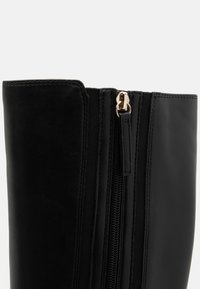 Black leather ankle boot with a textured finish. Features a side zipper with gold hardware and elastic fabric for fit.