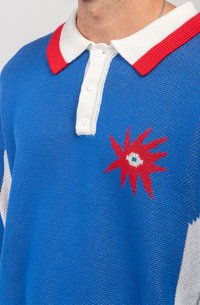 Polo din tricot de culoare albastră cu guler alb și accente roșii. Prezintă un design brodat colorat care seamănă cu o stea pe piept.