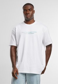 White cotton t-shirt featuring a loose fit, round neck, and printed text in blue: "Appreciate EVERYTHING Expect NOTHING."