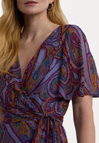 Robe enveloppante à motifs dans des teintes de violet et de bleu, ornée de motifs paisley, avec des manches courtes volantées et une taille cintrée par un lien.