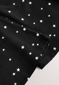 Mustast kangast, millel on valge tähemustri muster, kus väikesed ja keskmise suurusega tähed on ühtlaselt jaotatud kogu pinna ulatuses. Sile tekstuur.