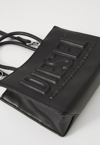 Borsa a tracolla in pelle nera con logo "DIESEL" in rilievo. Presenta due manici superiori e una chiusura con zip, texture liscia e forma strutturata.