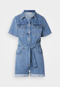 Combinaison courte en denim bleu à manches courtes, avec boutons à l'avant, poches poitrine, shorts retroussés et ceinture en tissu assorti nouée à la taille.