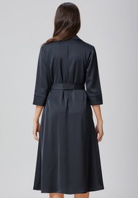 Robe en satin noir avec des manches trois-quarts, une taille ceinturée et une jupe fluide, présentant une texture lisse et un design minimaliste.