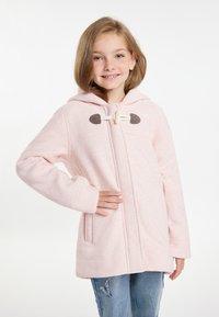 Giacca con cappuccio rosa chiaro con chiusura a toggle in legno e dettagli marroni. Presenta un materiale testurizzato e due tasche laterali. Abbinata a jeans di denim.