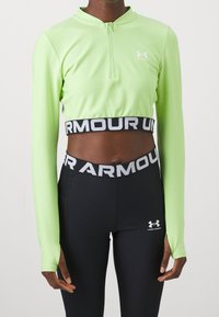 Hellgrünes, langärmliges Crop-Top mit Halbreißverschluss-Kragen, kombiniert mit schwarzen, figurbetonten Leggings mit einem Logo-Band an der Taille.