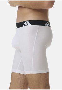 Weiße Boxer Shorts mit einem schwarzen Bund, der drei weiße Streifen aufweist. Hergestellt aus einem glatten, dehnbaren Material für hohen Tragekomfort.