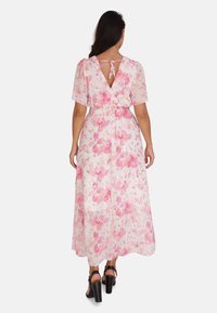 Robe maxi en tissu transparent avec un motif floral dans des tons de rose, dotée d'une taille smockée et d'un dos en V maintenu par un lien. Talons noirs.
