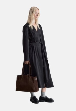Black wrap dress with long sleeves and a belted waist, complemented by a dark brown suede tote bag and black leather shoes with chunky soles.