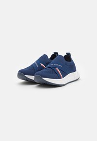 Mörkblå mesh-sneakers med vit sula. Har en korsrem med röda och vita ränder samt en logotyp på sidan. Lätt och andningsbar design.