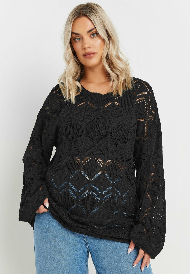 Svart stickad tröja med ett openwork geometriskt mönster, lösa långa ärmar och rundad halsringning, tillsammans med blå jeans.