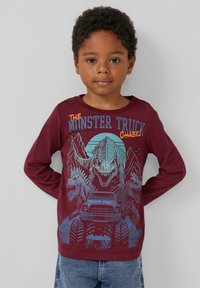 Burgunderrotes Langarmshirt mit einer Grafik von zwei Dinosauriern und einem Truck, mit blauen und orangefarbenen Text, der "DER MONSTERTRUCK-JÄGER!" sagt.